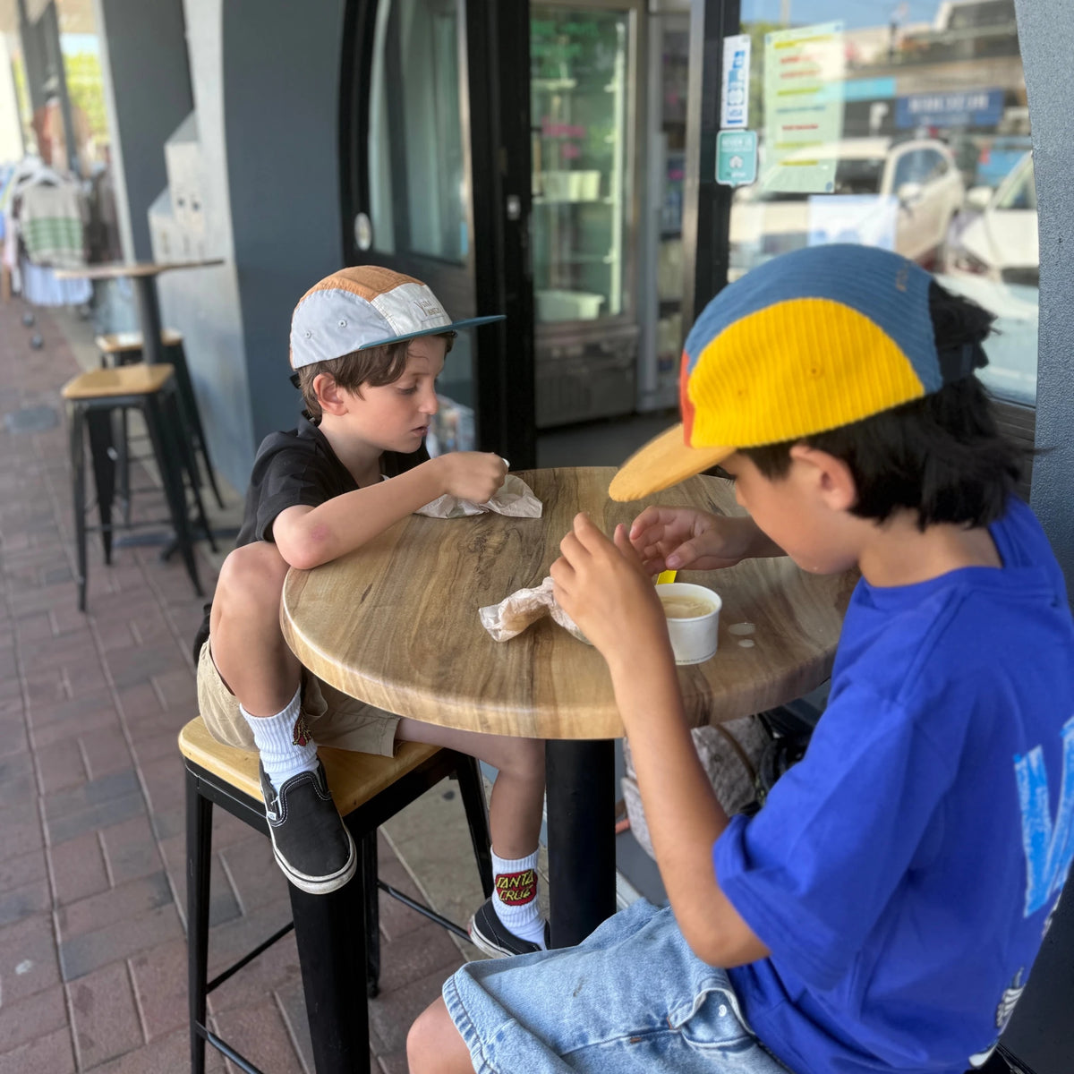 2 boys having ice-cream wearing a 5 panel nylon hat and a 5 panel cordurou hat