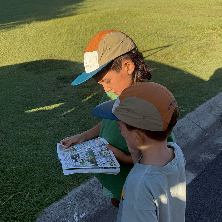 2 boys wearing Family matching nylon 5 panel cap in earthy blue while reading a comics book - Stick Hunters