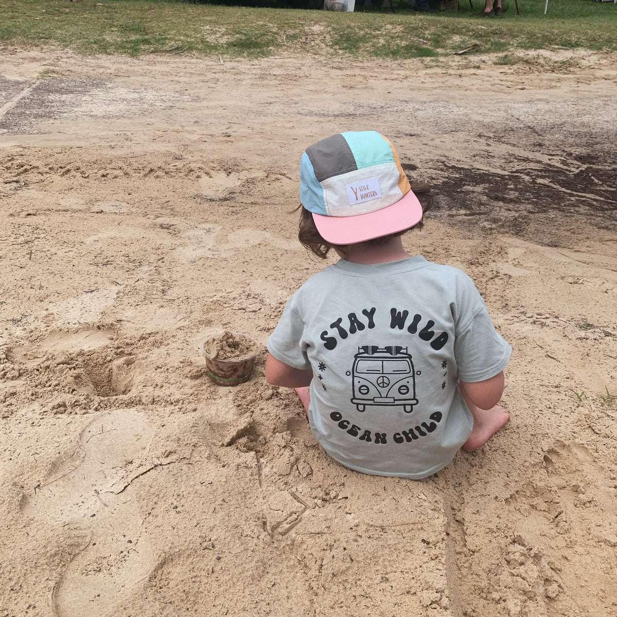 Toddler playing in the sand with a nylon 5 panels hat and a ocean inspired box tee.