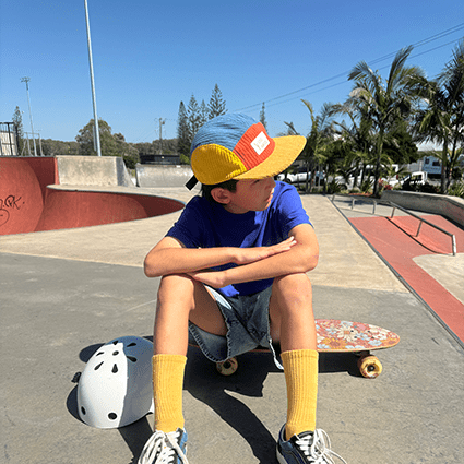 Boy sitting at a skatepark family matching corduroy 5 panel cap in primary colours - baby to adult sizing - Stick Hunters